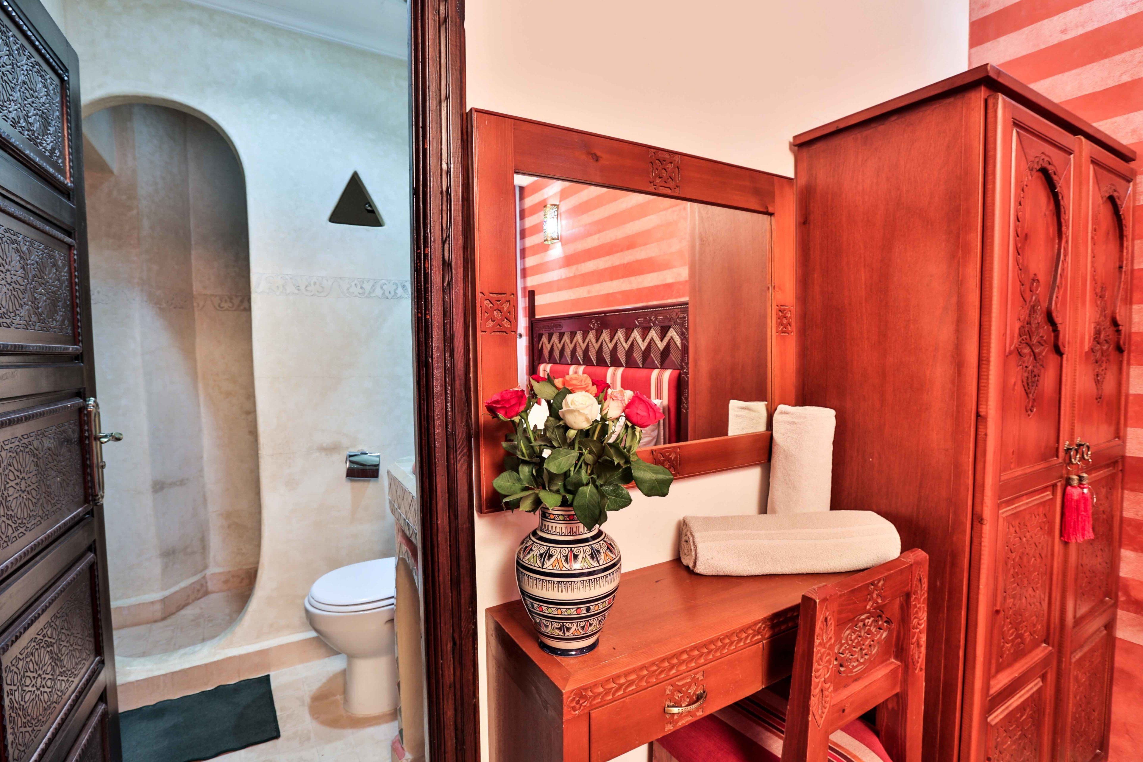 A bathroom with a wooden vanity, a mirror, a vase with flowers, and a towel on the counter.