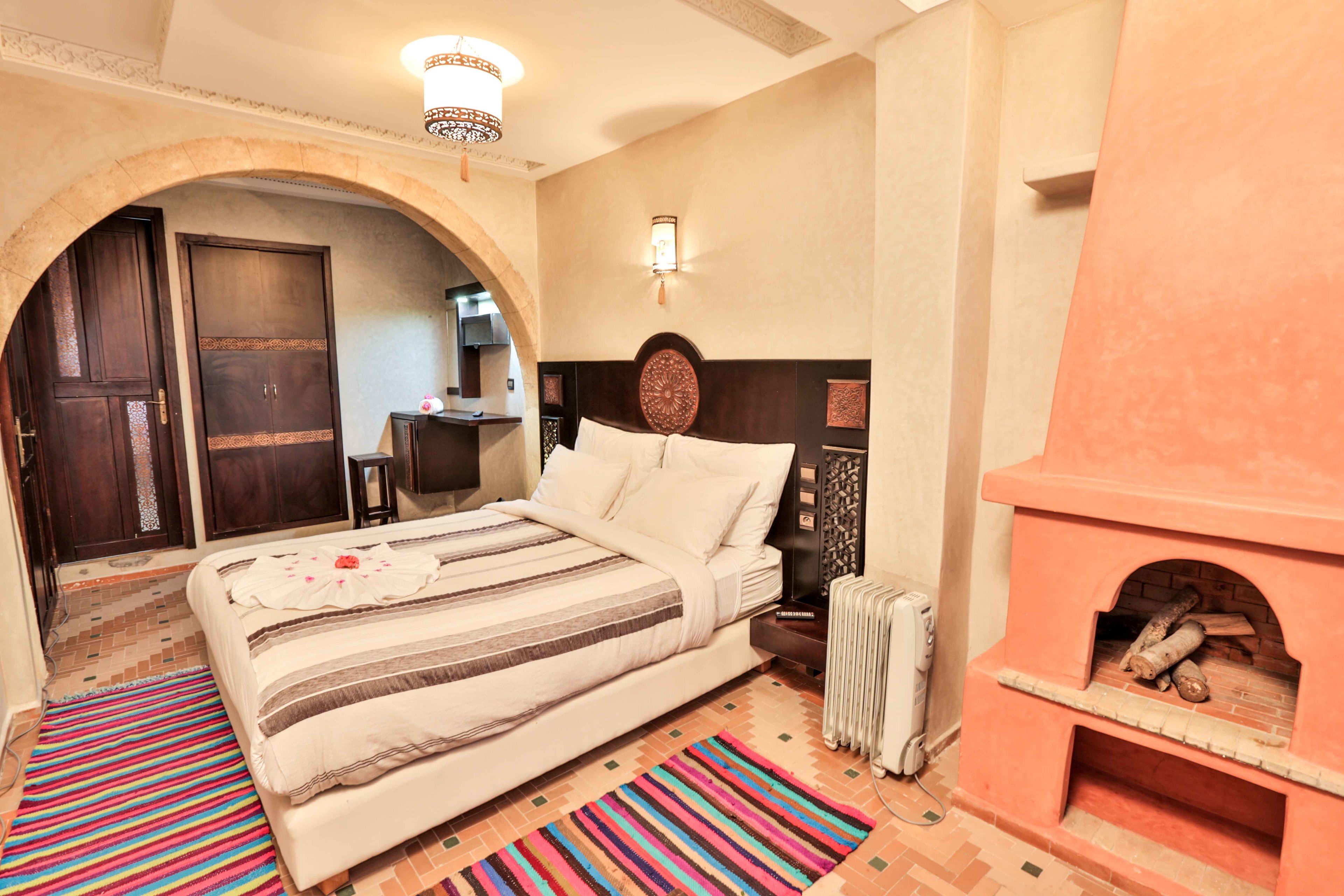 A bedroom with a bed, a fireplace, a tiled floor, and an arched doorway.