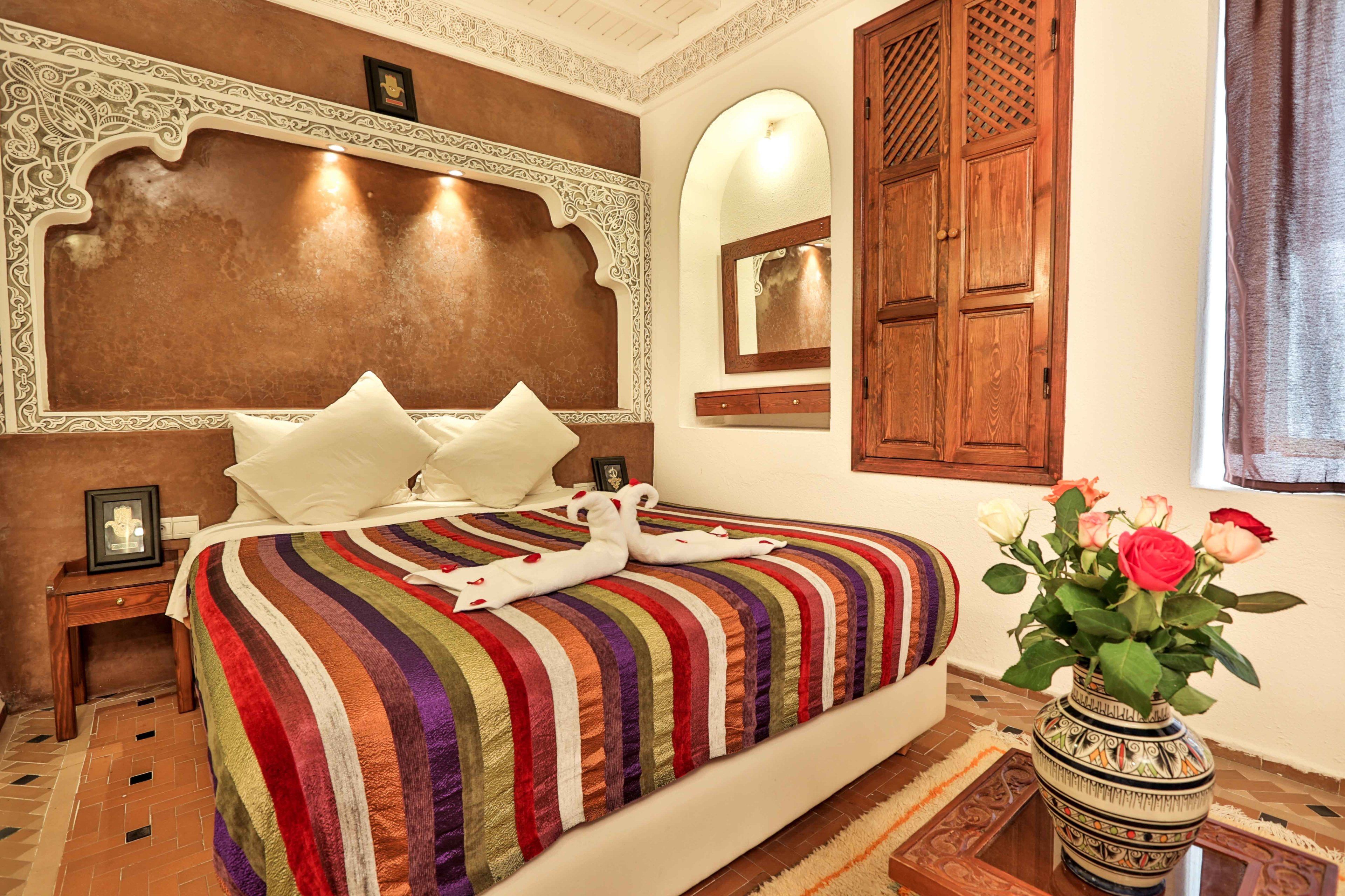 A hotel room with a large bed, a wooden headboard, a mirror, and a vase with flowers.