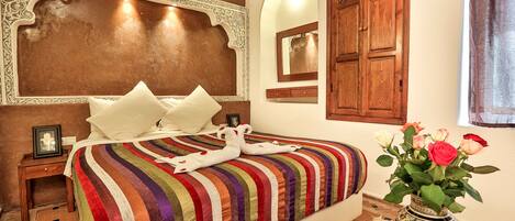 Habitación de hotel con una cama grande, cabecera de madera, un espejo y un jarrón con flores.