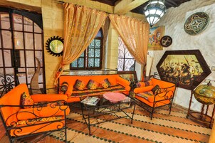 Una habitación con sofás naranja, una mesa de centro de vidrio, baldosas con diseño y decoración en la pared.