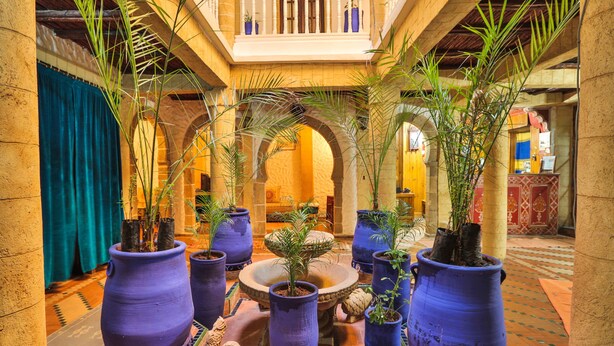 A courtyard with large potted plants, a central fountain, and a balcony overlooking the area. - Riad Nakhla (Essaouira)