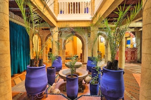 A courtyard with large potted plants, a central fountain, and a balcony overlooking the area. - Riad Nakhla (Essaouira)