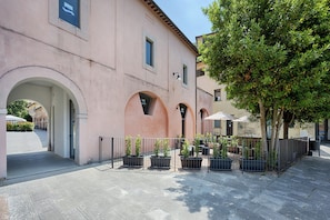 A pink building with arched doorways and a paved courtyard with potted plants. - Siena Vip (Siena)