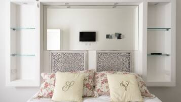 Un dormitorio con cama, almohadones decorativos, televisor montado y estanterías empotradas.