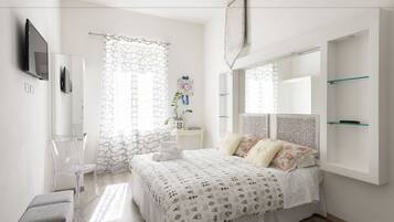 A modern bedroom with a large bed, a TV mounted on the wall, and a small side table with a plant.