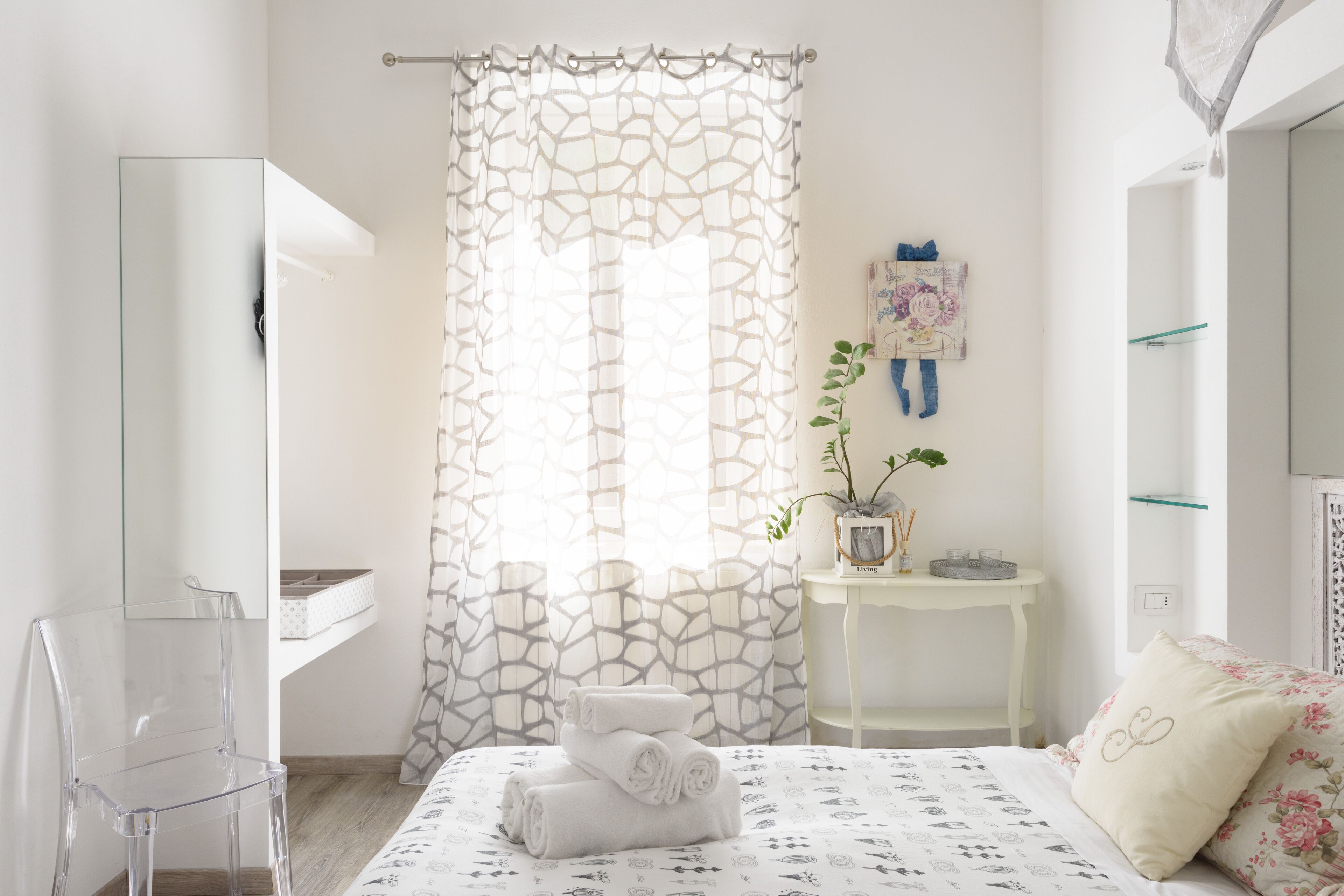 A modern bedroom with a bed, a clear chair, a small table with a plant, and a shower area.