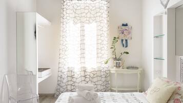 A modern bedroom with a bed, a clear chair, a small table with a plant, and a shower area.