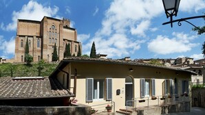 A historic building with a prominent tower and arched windows, situated in a town with traditional architecture and a clear blue sky.