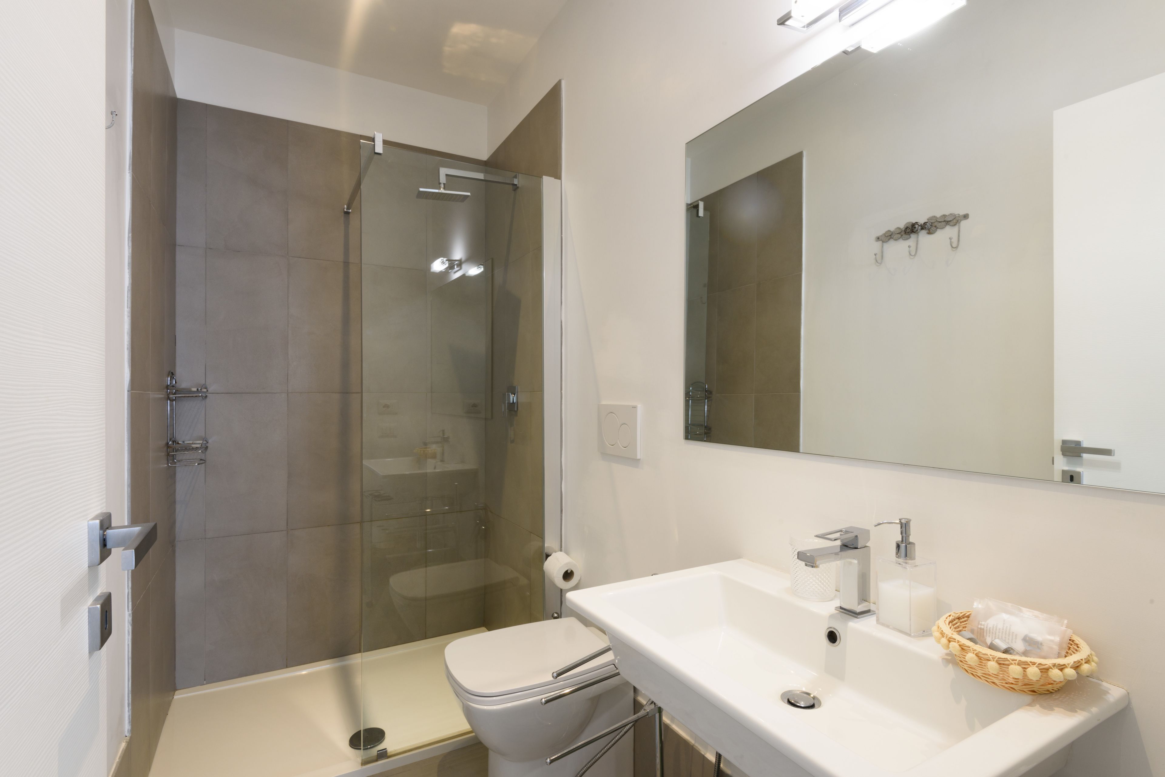 Une salle de bain moderne avec une douche à parois de verre, un lavabo blanc doté d’un distributeur de savon et un miroir au-dessus du lavabo.