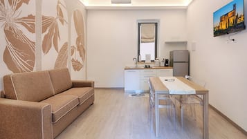 Une pièce moderne comprenant un canapé, une table à manger avec des chaises, un coin cuisine avec un réfrigérateur et un téléviseur fixé au mur.