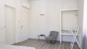 A bedroom with a bed, a grey armchair, a white wardrobe, and a white shelf with storage boxes.
