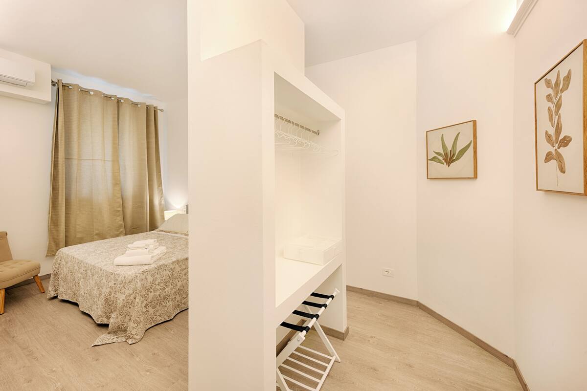 Ein Schlafzimmer mit Bett, einer Bank, einem Kleiderhaken und einem kleinen Regal.