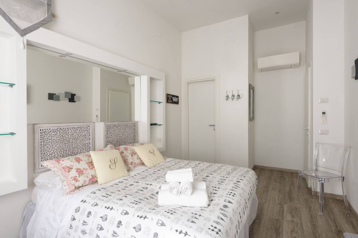 Ein modernes Hotelzimmer mit einem großen Bett, einem Spiegel, einem Kleiderschrank und einem transparenten Stuhl.