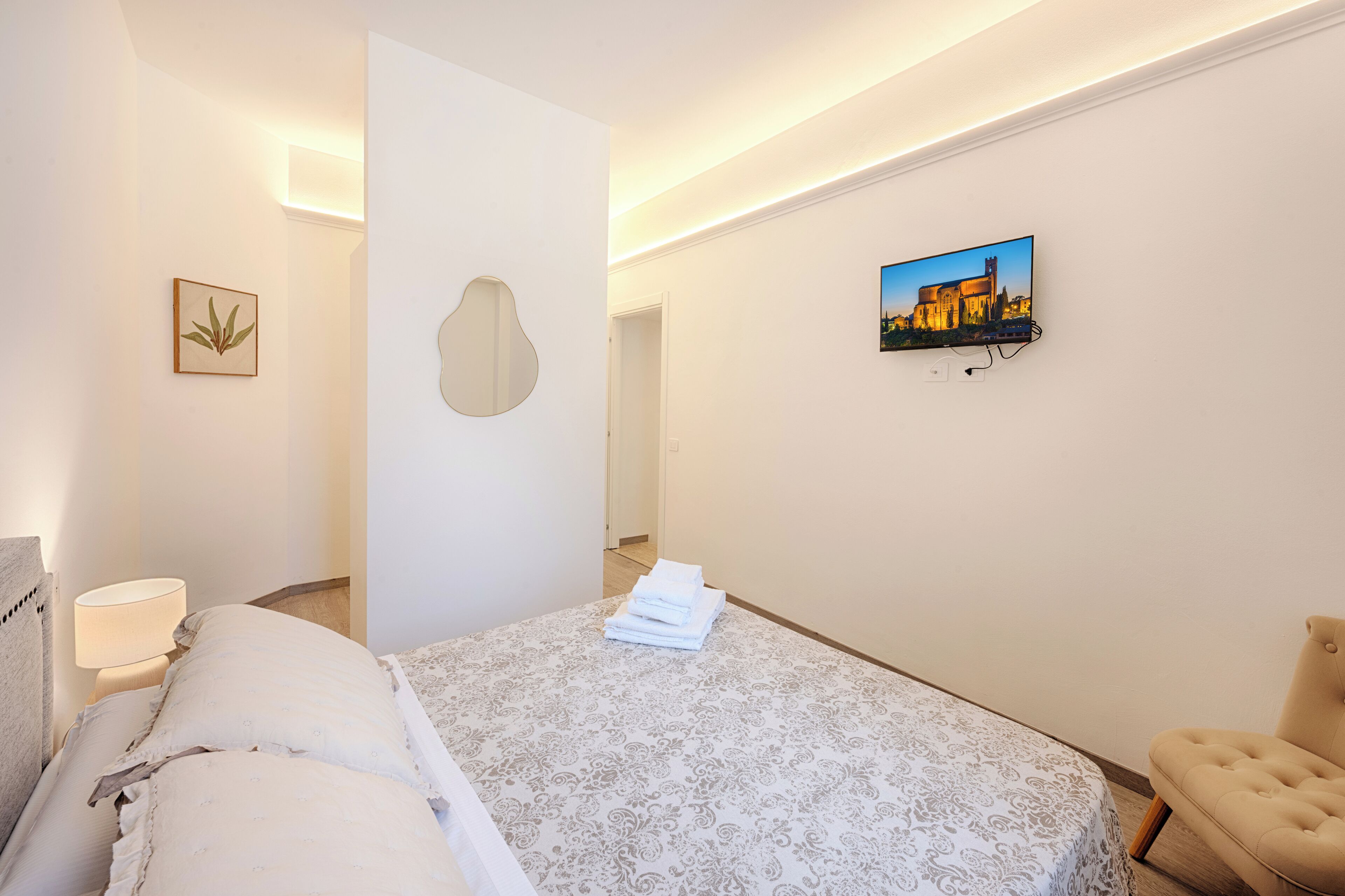 A hotel room with a bed, a chair, a TV, and a wall-mounted picture.