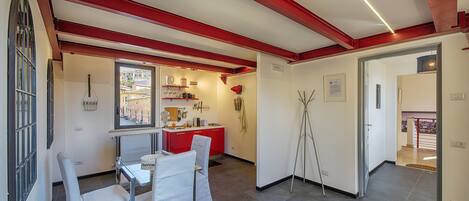 A modern kitchen with red accents, a dining area with white chairs, and a view through a window.