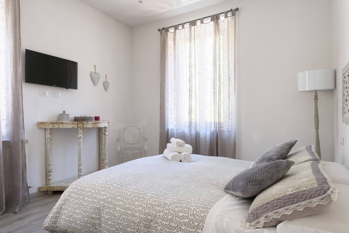 Ein Schlafzimmer mit einem Bett, einem an der Wand montierten Fernseher, einem kleinen Tisch und einem Stuhl.
