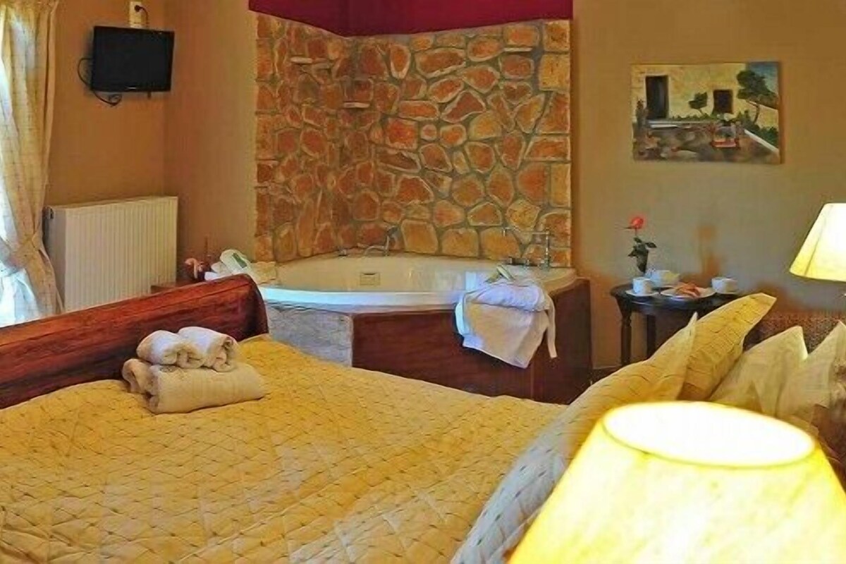 A hotel room with a bed, a bathroom with a bathtub, a window with curtains, and a painting on the wall.