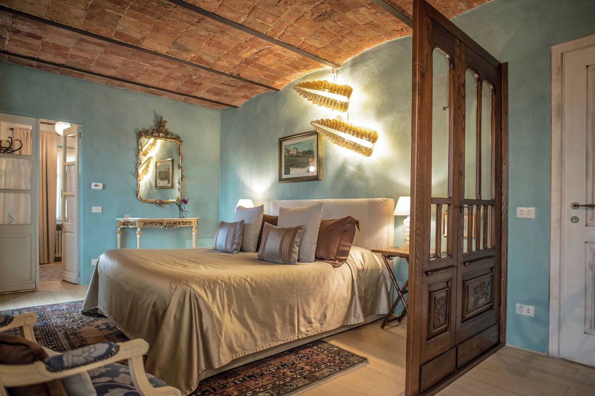 A bedroom with a large bed, a wooden wardrobe, a mirror, and a chandelier.