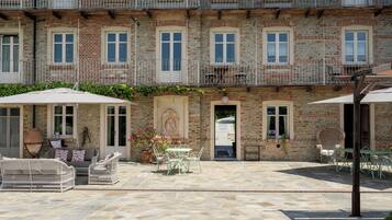 Un patio con mobiliario exterior, suelo de piedra y un edificio con múltiples ventanas y balcones.