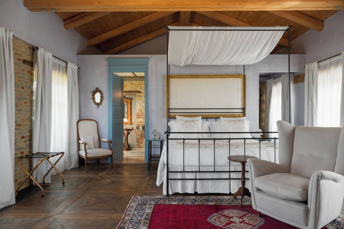 A bedroom with a bed, a chair, a small table, and a hanging canopy.