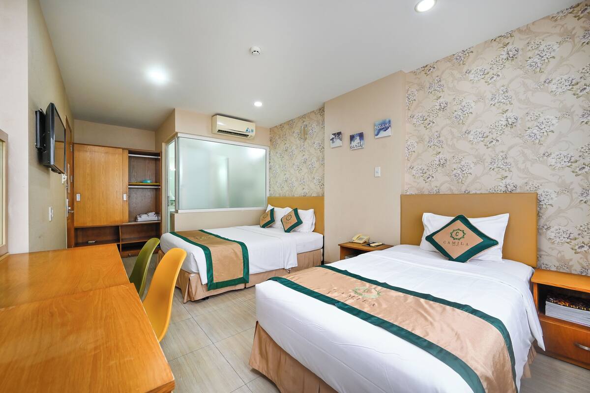 A hotel room with two beds, a wooden table, a TV, a wardrobe, and a wall-mounted air conditioner.
