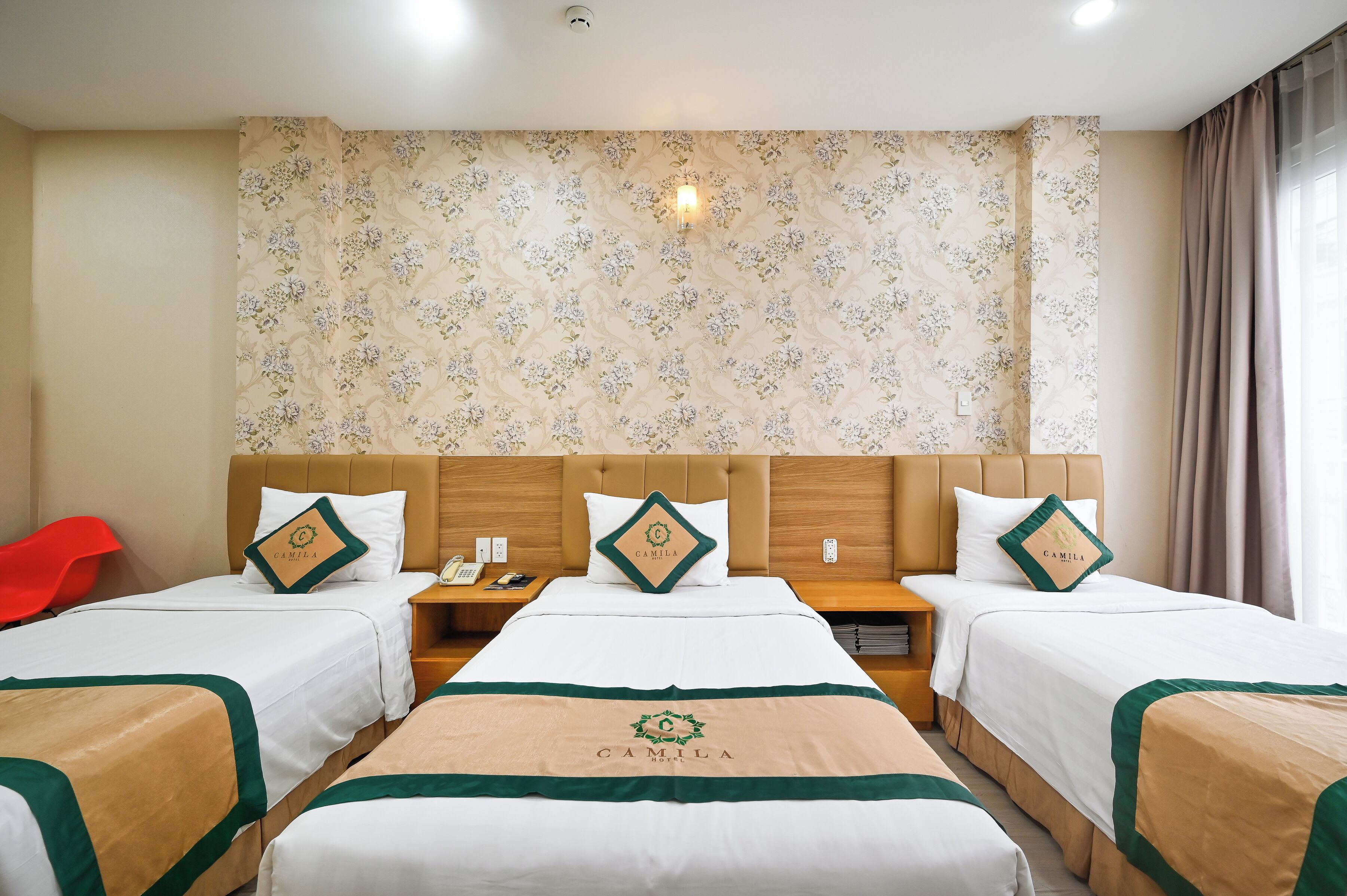 A hotel room with four beds, floral wallpaper, and a nightstand with a phone and a lamp.