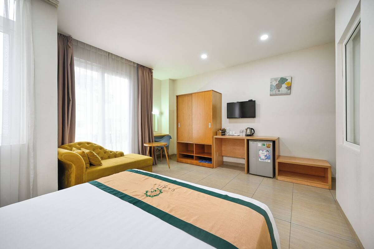 A hotel room with a bed, a yellow sofa, a desk with a computer, a television, and a small refrigerator.