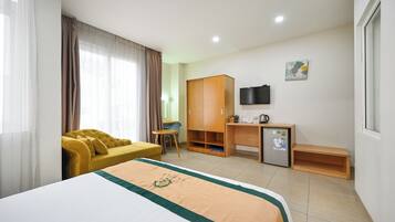 A hotel room with a bed, a yellow sofa, a desk with a computer, a television, and a small refrigerator.
