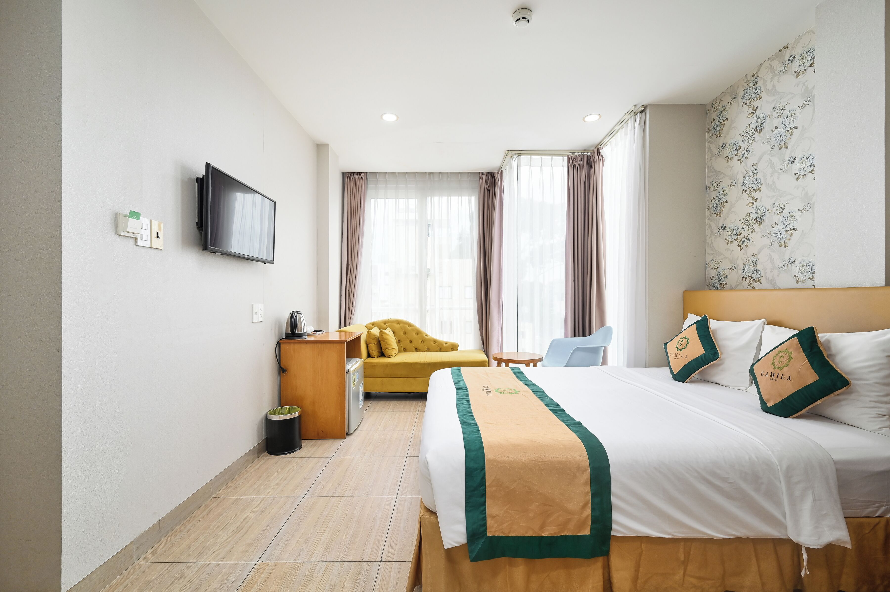 A hotel room with a bed, a sofa, a desk, a television, and a trash bin.