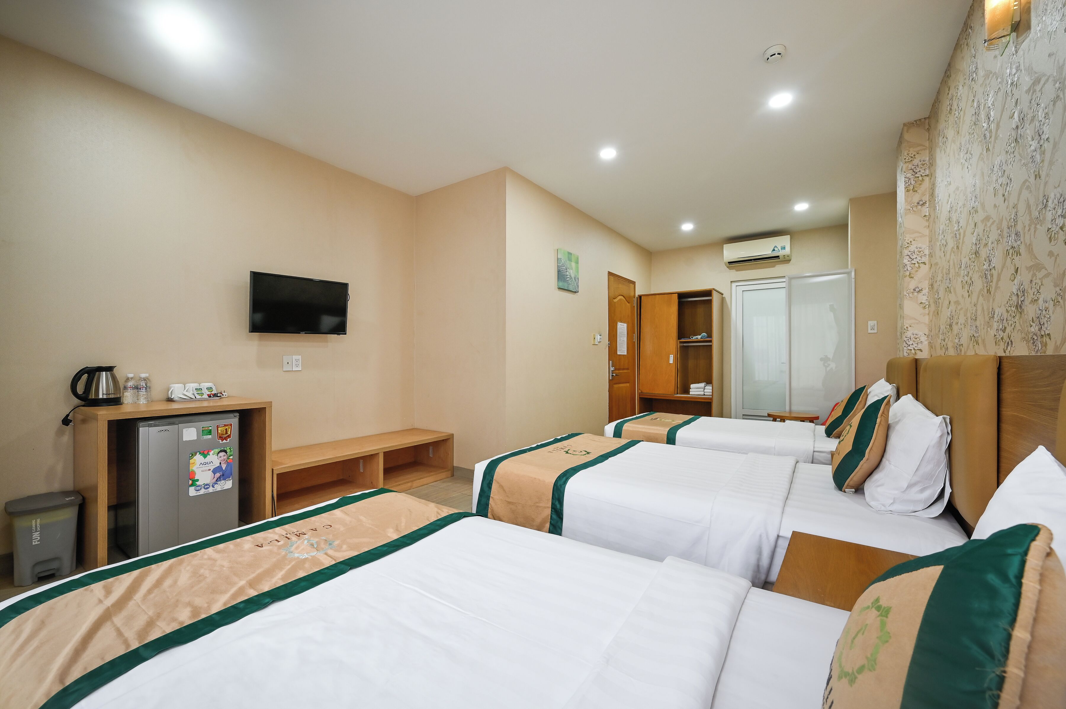 Una habitación de hotel con tres camas, televisión, escritorio con refrigerador y armario.