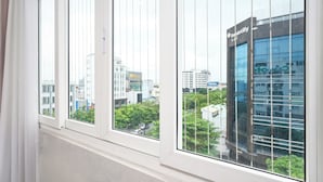 A view from a window with white blinds, overlooking a cityscape with modern buildings and a river.