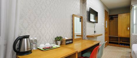 Una habitación de hotel con un escritorio de madera, un espejo, un televisor montado en la pared, un armario y una cama.
