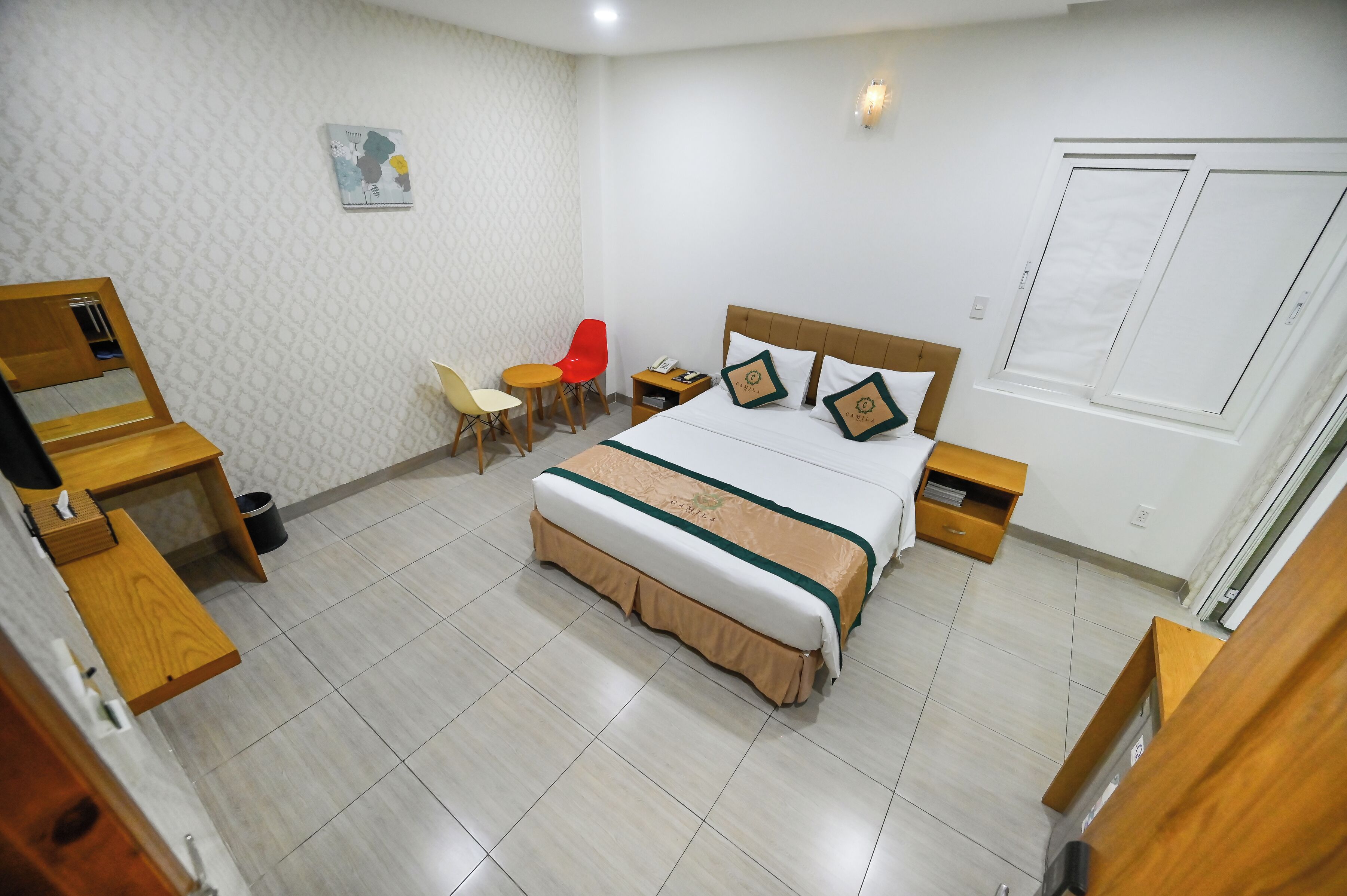 A hotel room with a bed, bedside tables, a desk, a chair, and a small table with a chair.