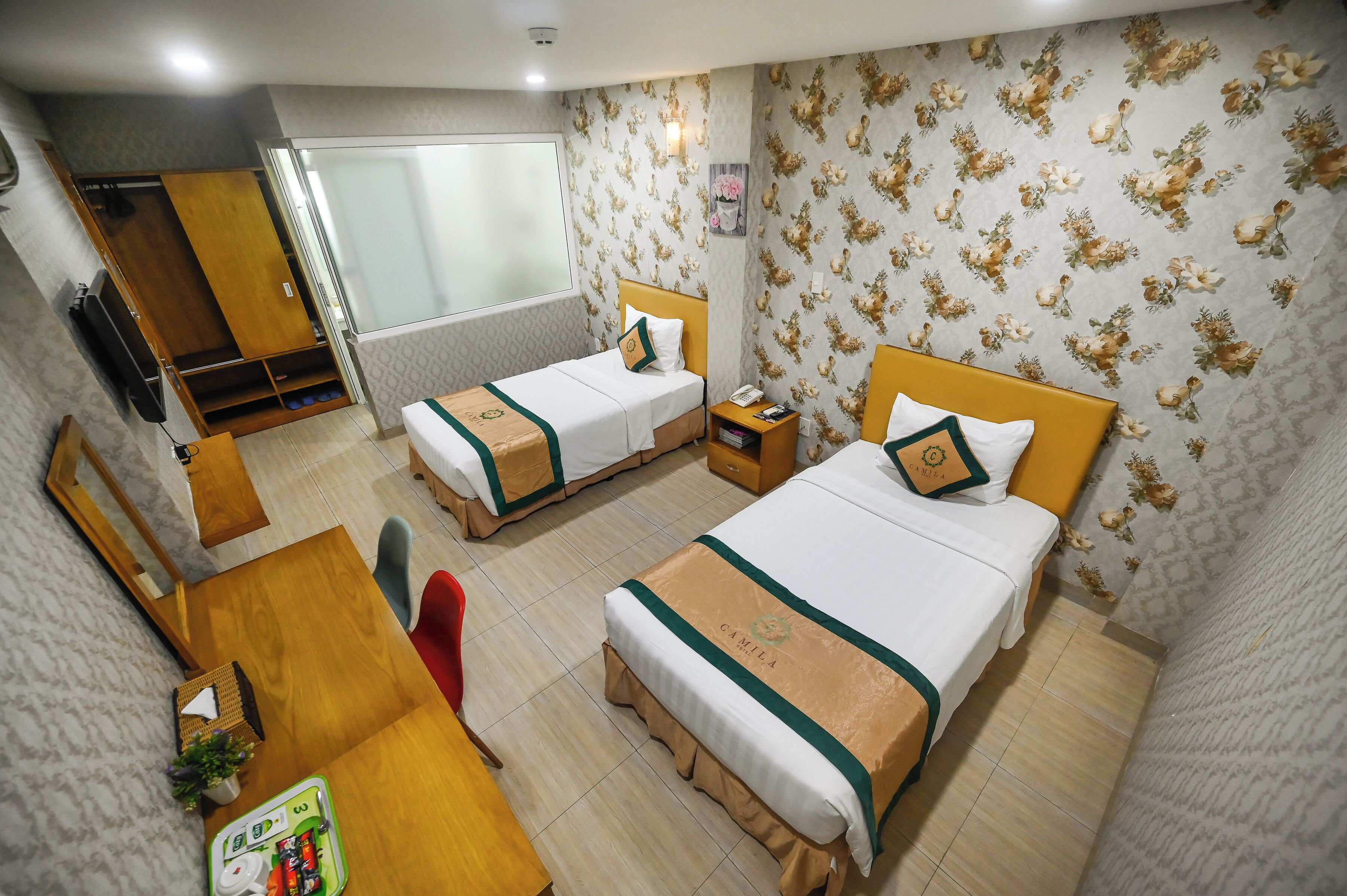 A hotel room with two beds, a desk, a chair, a TV, and a wardrobe.