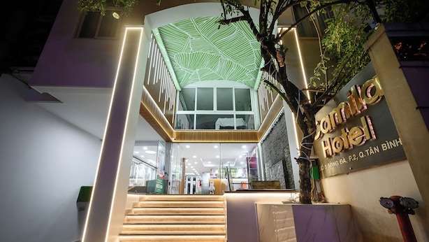 A hotel entrance with a staircase leading to a second-floor balcony, a sign reading "Hotel Quell," and a tree in the foreground.