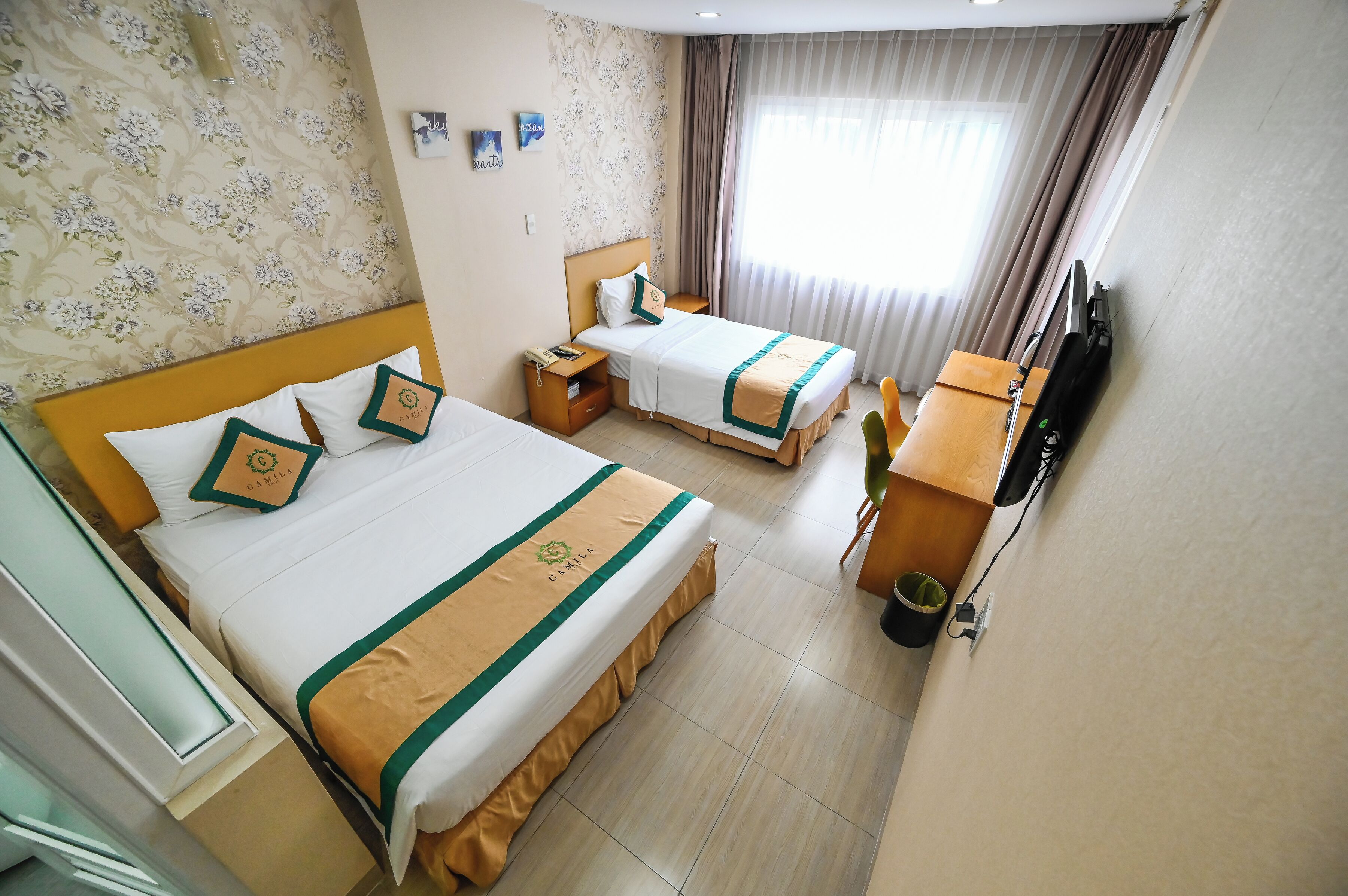A hotel room with two beds, a desk, a TV, and a window with curtains.