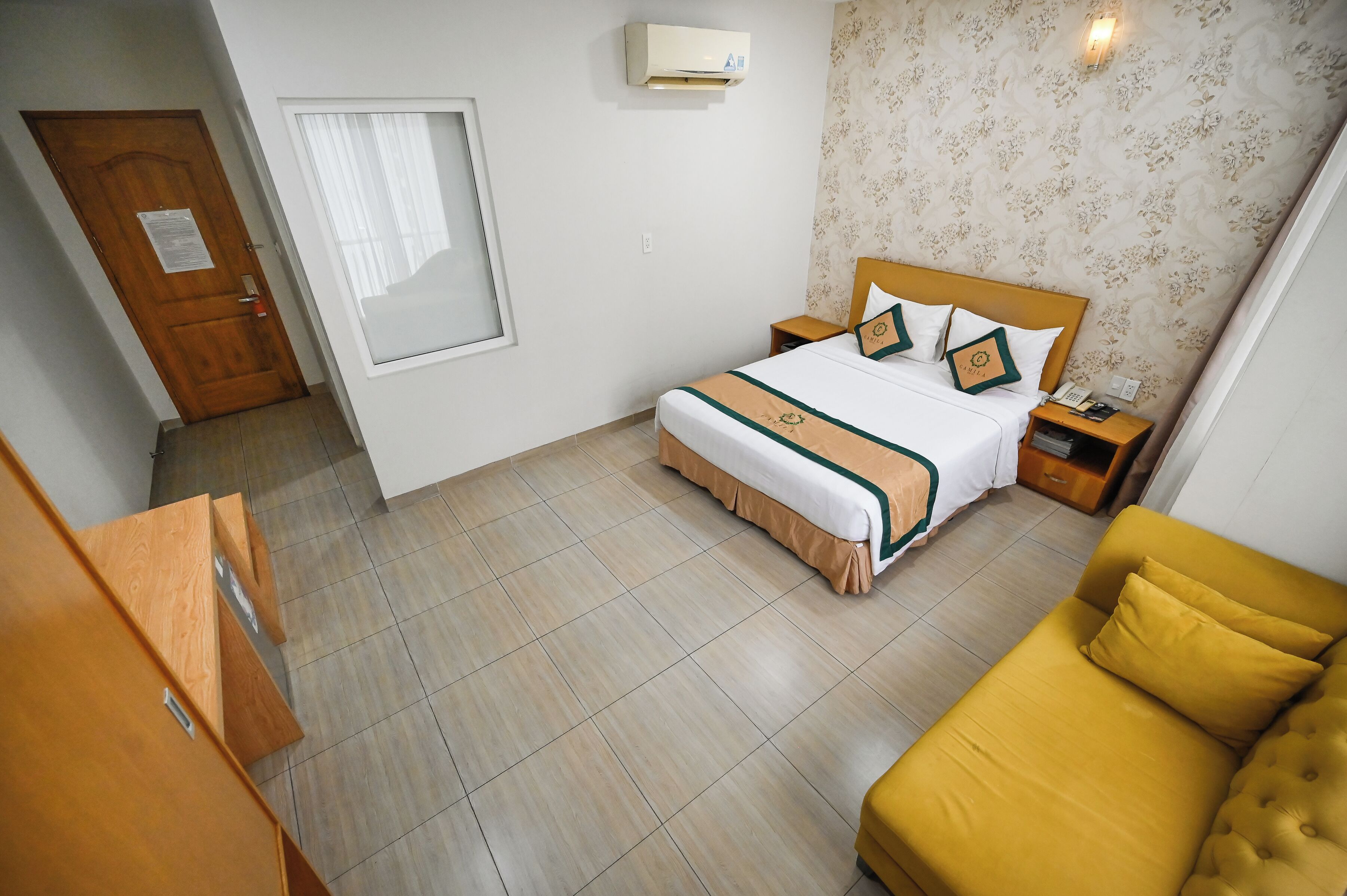 A hotel room with a bed, a nightstand, a sofa, a wooden wardrobe, and a window.