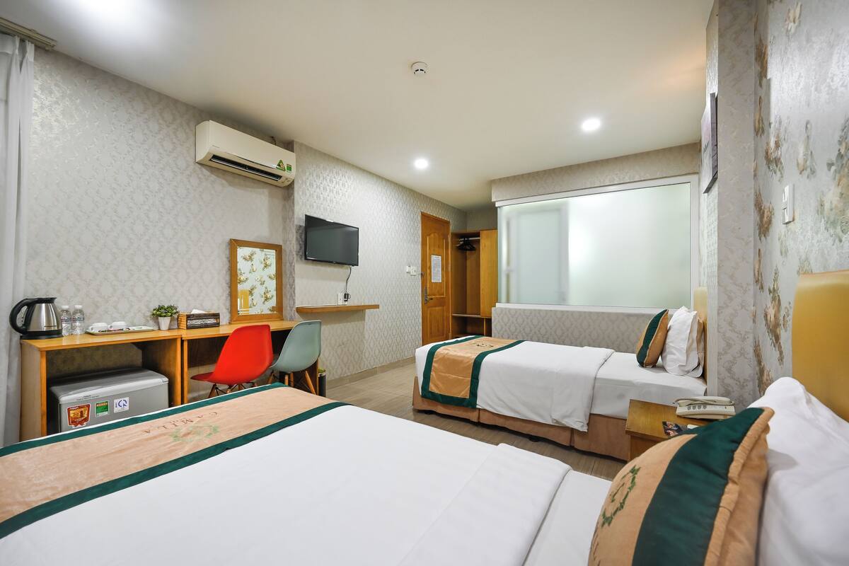 A hotel room with two beds, a desk with a chair, a television, and a window with a view.
