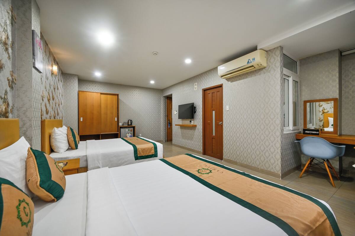 A hotel room with two beds, a desk, a chair, an air conditioner, a television, and a wardrobe.