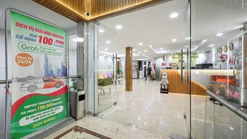 A hotel lobby with a glass door entrance, a reception desk, and a sign advertising airport transfer services.