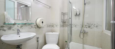 Et badeværelse med en hvid vask, toilet og badekar, et brusekabine i glas samt et spejl med sæbedispenser.