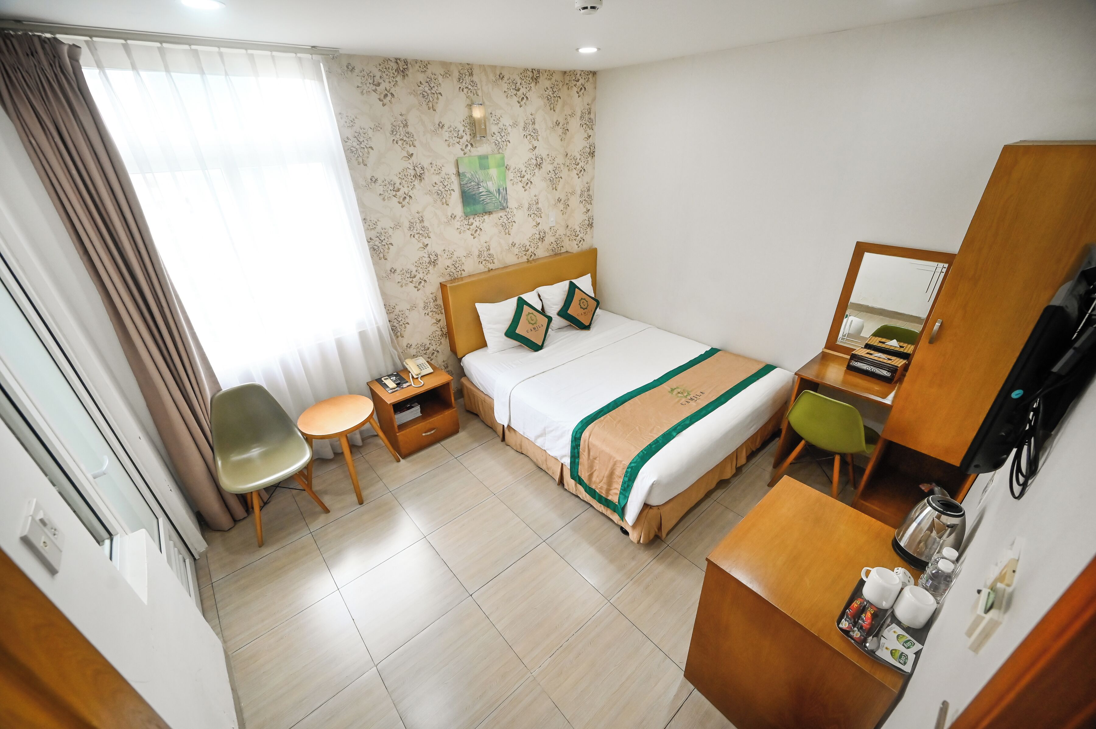 Ein Hotelzimmer mit Bett, Schreibtisch, Stuhl, kleinem Tisch, Nachttisch und einem Fenster mit Vorhängen.