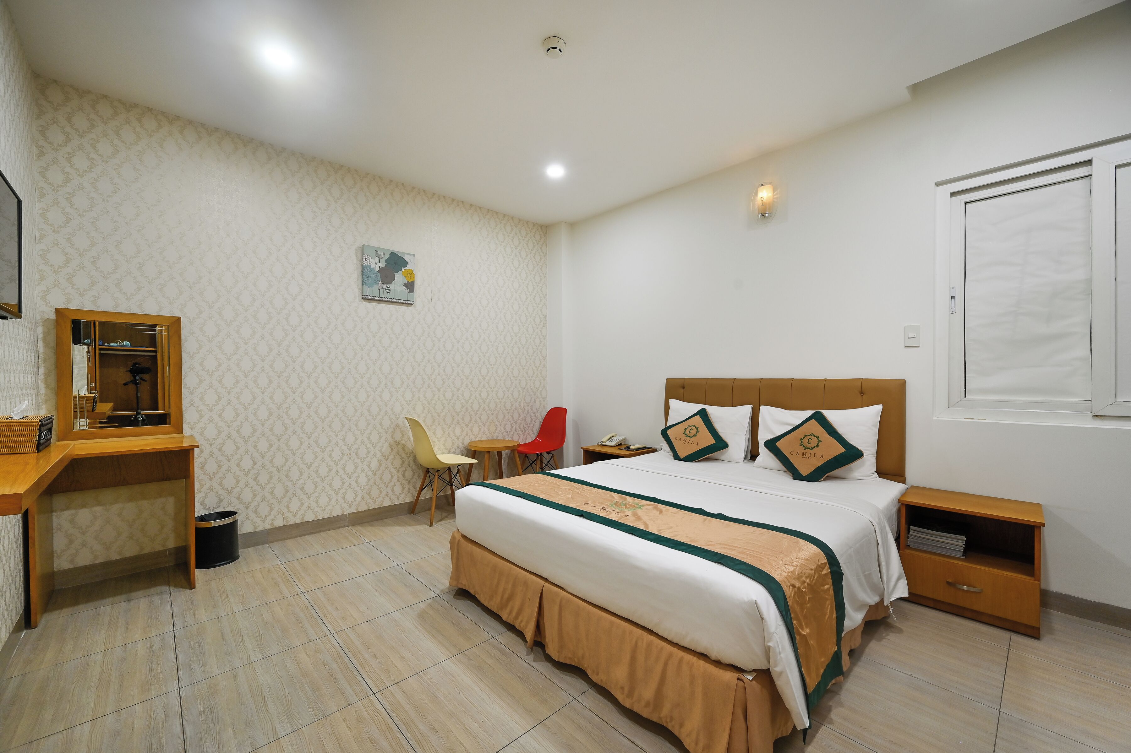 A neatly arranged bedroom with a bed, bedside table, desk, chair, and a small trash bin.