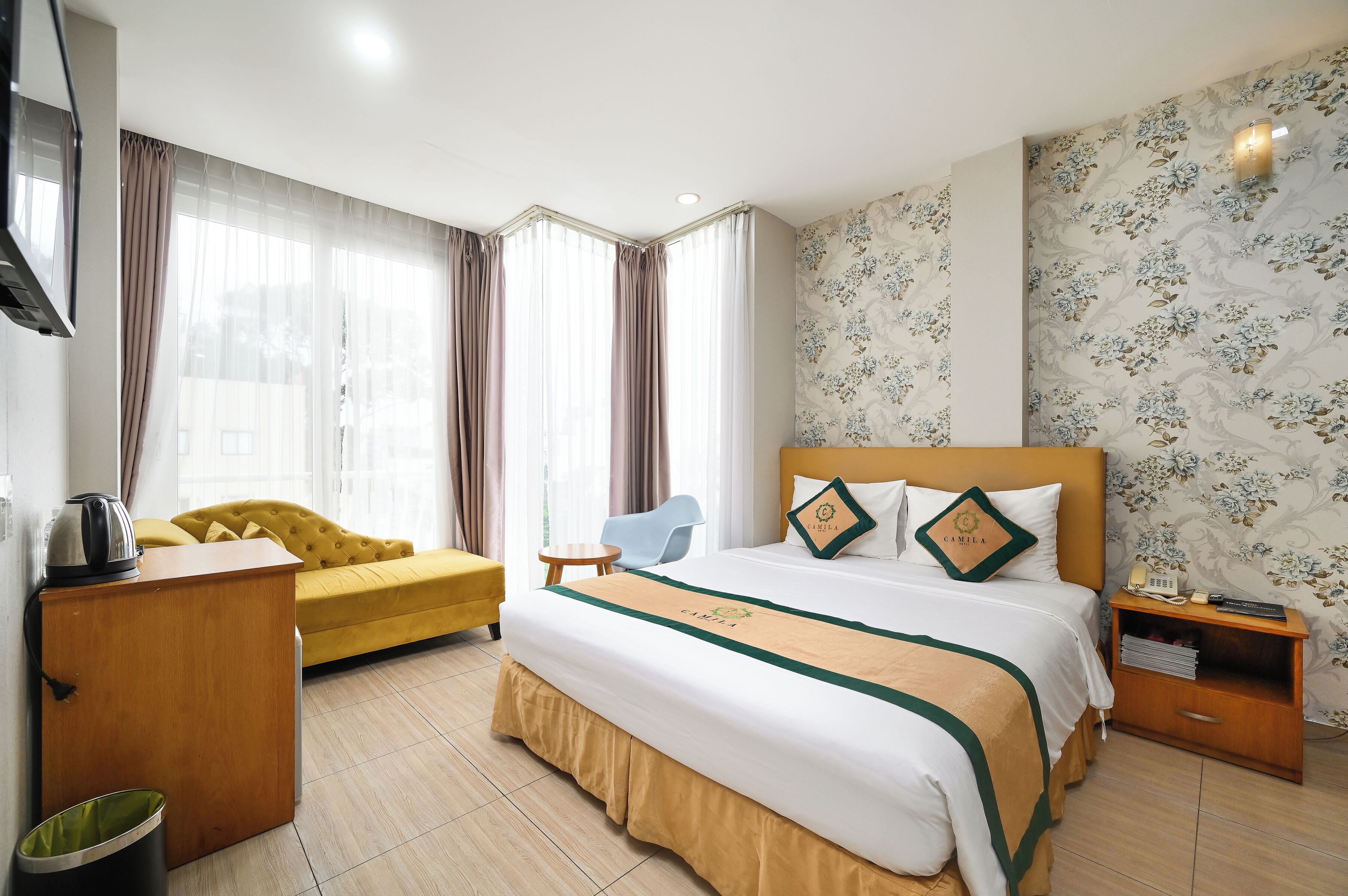 A hotel room with a large bed, a yellow sofa, a small table, and a TV.