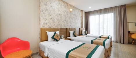Habitación de hotel con tres camas, una silla roja, un escritorio y un ventanal con cortinas.