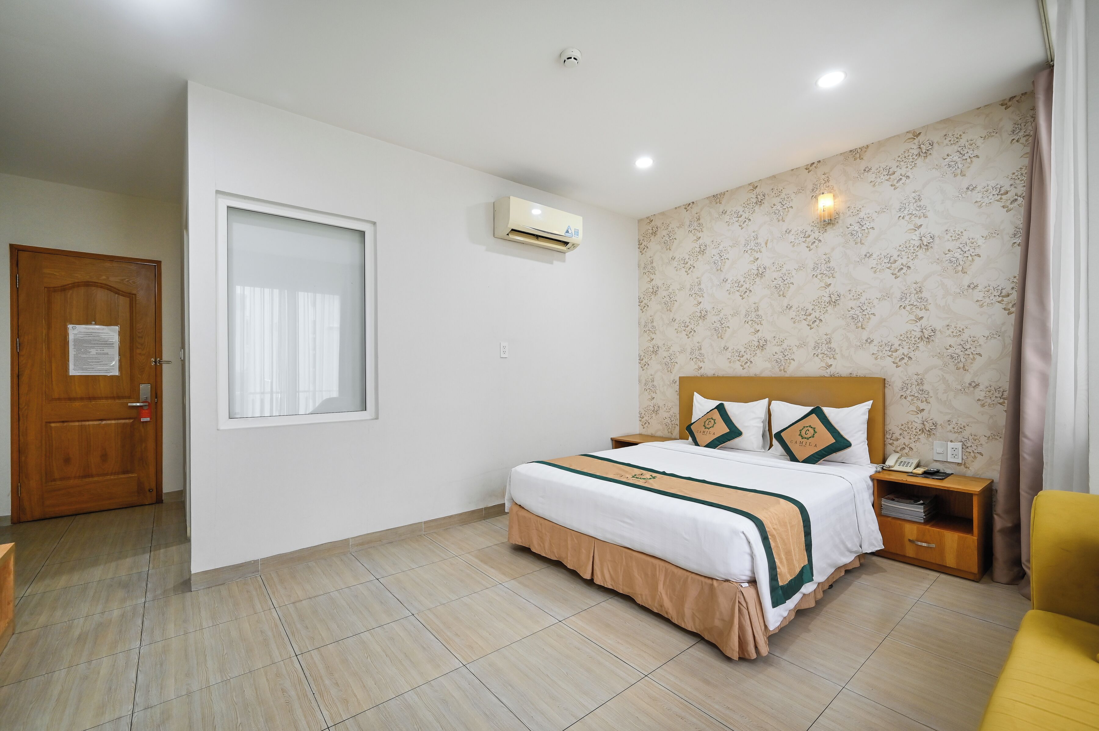 Una camera d'albergo con un letto, un comodino, una sedia, una porta e un condizionatore d'aria.