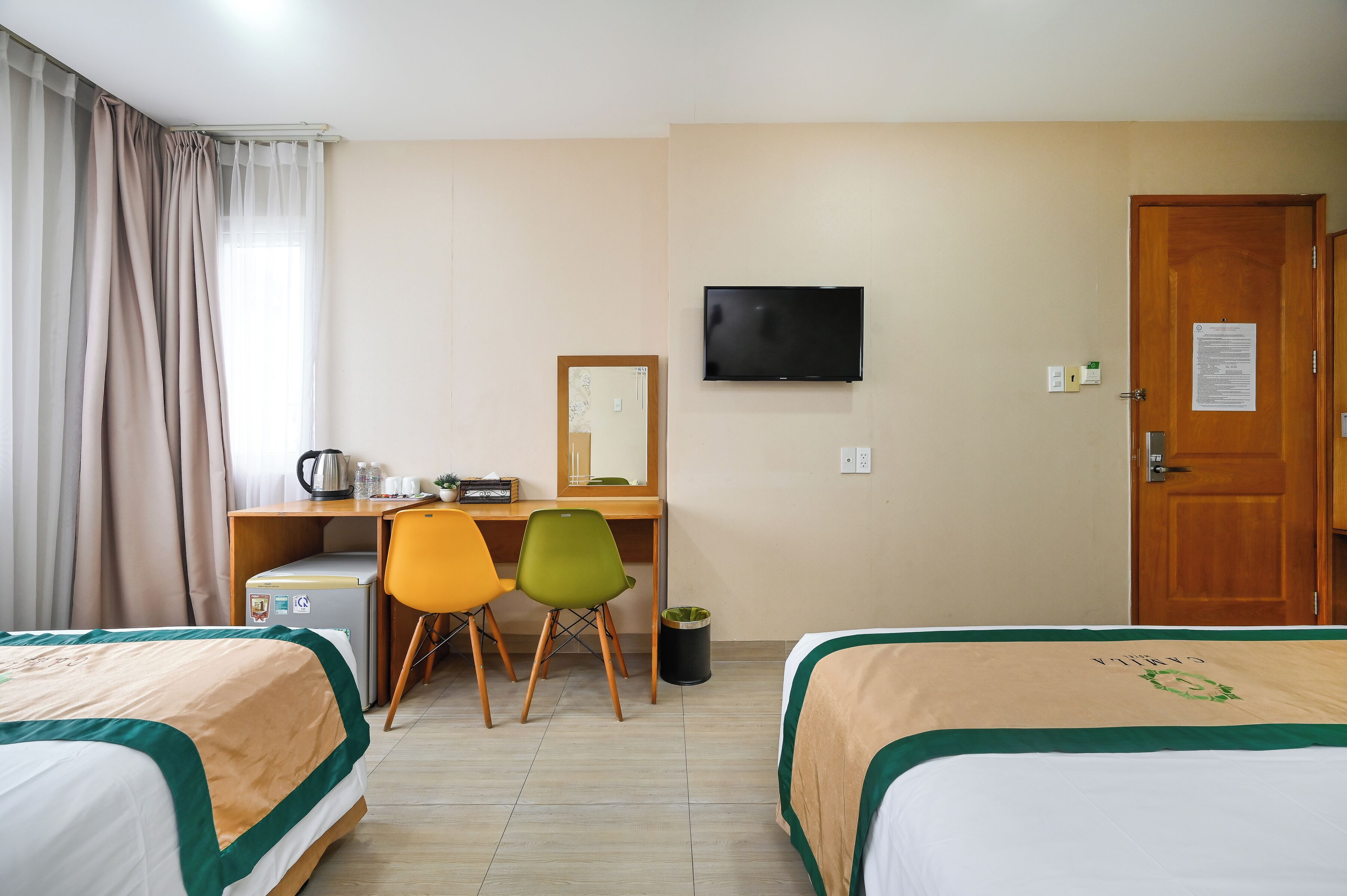 Een hotelkamer met twee bedden, een bureau met stoel, een televisie en een deur.