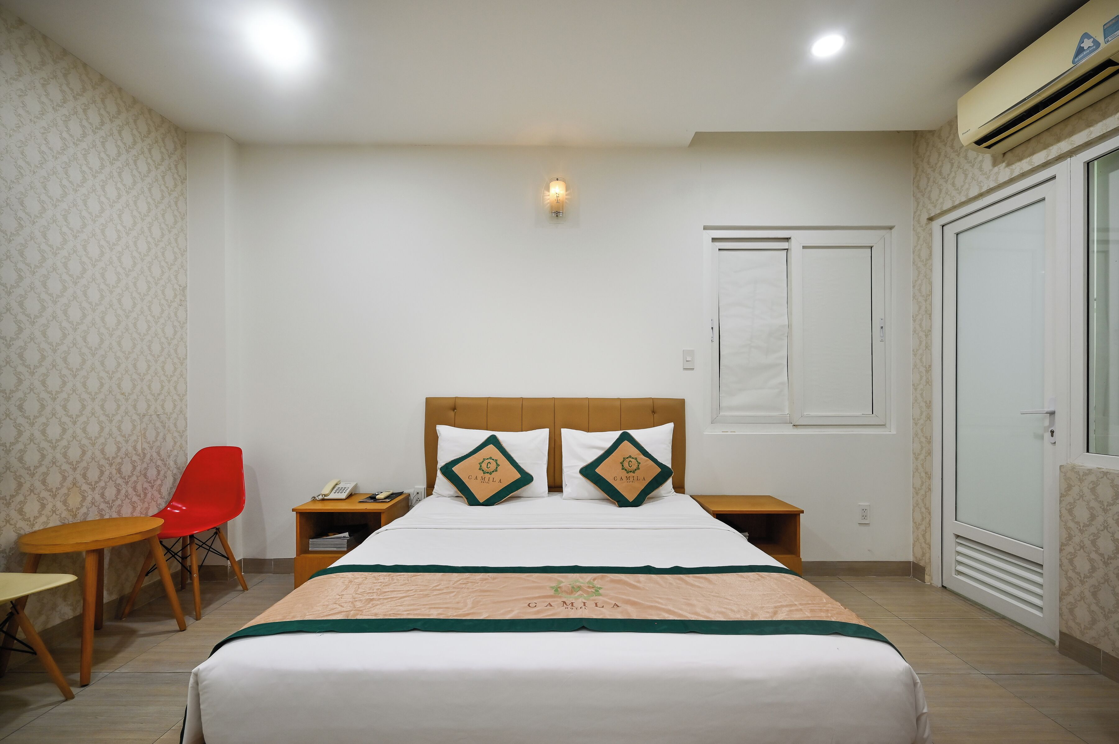 A hotel room with a bed, two nightstands, a red chair, a small table, and a wardrobe.