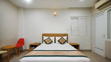 A hotel room with a bed, two nightstands, a red chair, a small table, and a wardrobe.